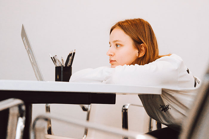 Young woman looking tired at laptop in a workplace, illustrating frustrating normal workplace practices wanted to disappear.