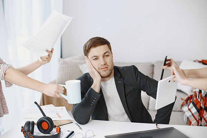Stressed man surrounded by multiple tasks showing common workplace practices that people want to disappear in the future.