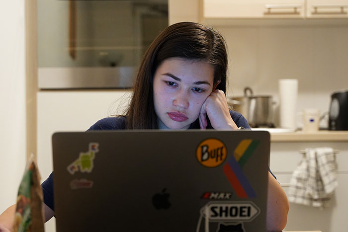 Young woman working late on a laptop, looking tired and frustrated with common workplace practices.