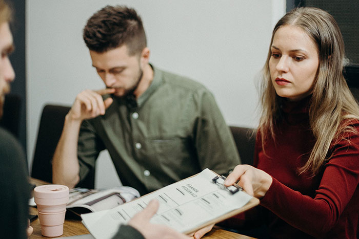 Three coworkers discussing documents during a meeting, illustrating common workplace practices and office dynamics.