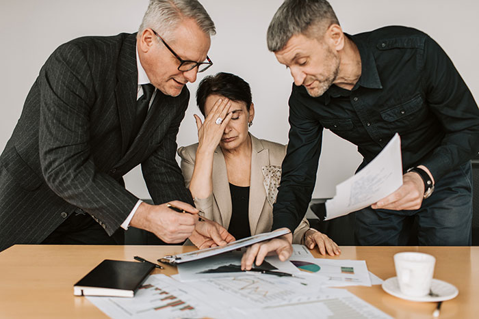 Three stressed colleagues reviewing documents in an office, illustrating common workplace practices people want to change.