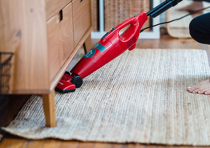 A Person Vacuuming a Carpet Under a Side Cabinet A Person Vacuuming a Carpet Under a Side Cabinet