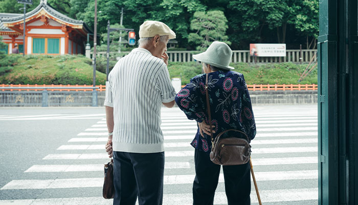 Elderly couple crossing a street, evoking thoughts on human longevity and ancient times linked to dinosaurs.