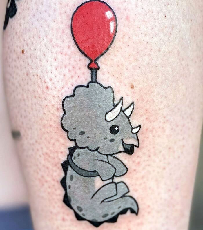 Cute dinosaur tattoo with balloon, perfectly executed on skin.