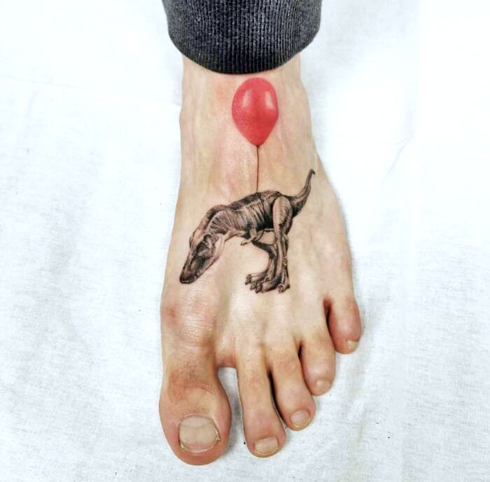 Dinosaur tattoo on a foot with a red balloon design.
