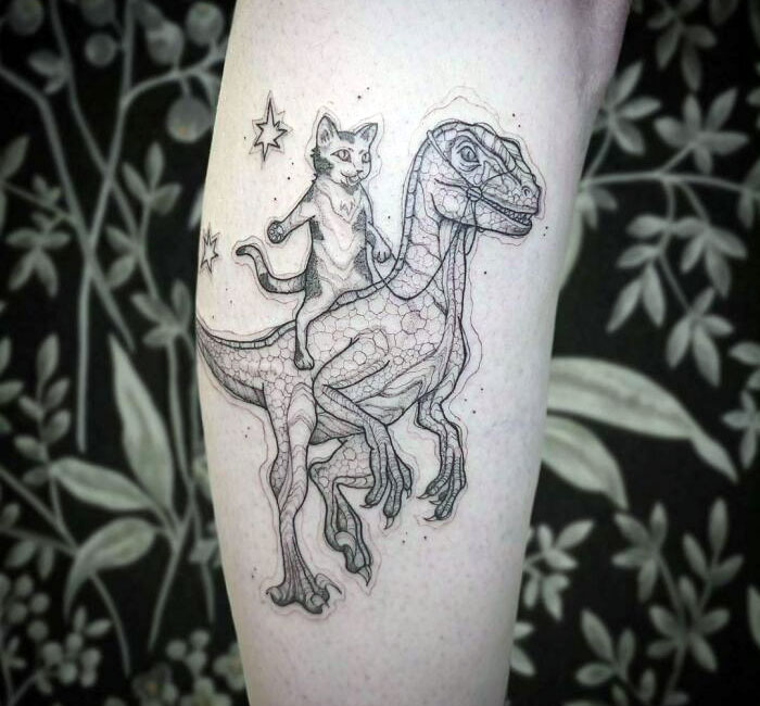 Cool dinosaur tattoo featuring a cat riding a dinosaur with stars, executed perfectly on the forearm.