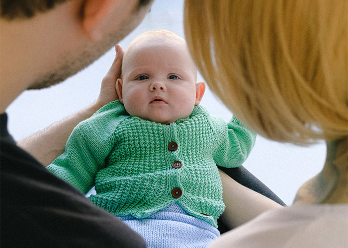 Parents holding a baby wearing a green sweater, highlighting outdated parenting myths and common misconceptions.