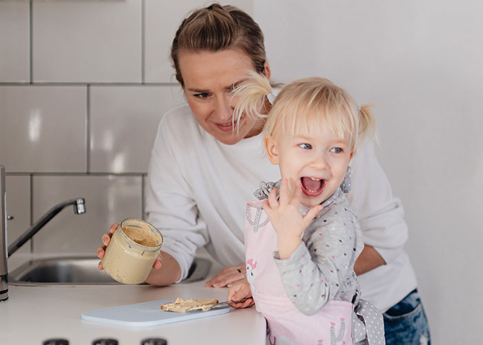 Mother and toddler daughter having fun in the kitchen debunking outdated parenting myths with healthy snacks.