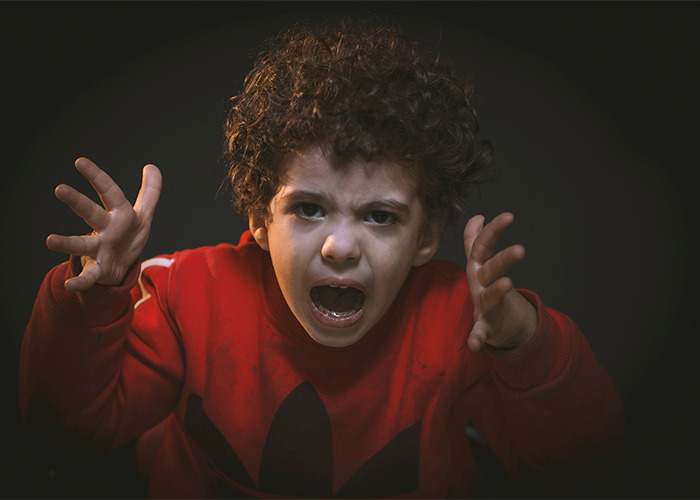 Angry young boy shouting and raising hands against a dark background illustrating outdated parenting myths.