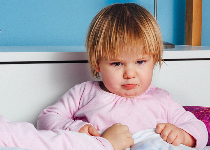 Young child in pink pajamas sitting on a bed, illustrating outdated parenting myths and common misconceptions.