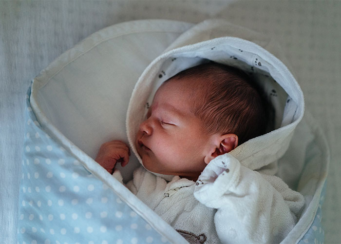 Newborn baby wrapped in a white blanket, peacefully sleeping, illustrating outdated parenting myths and child care beliefs.