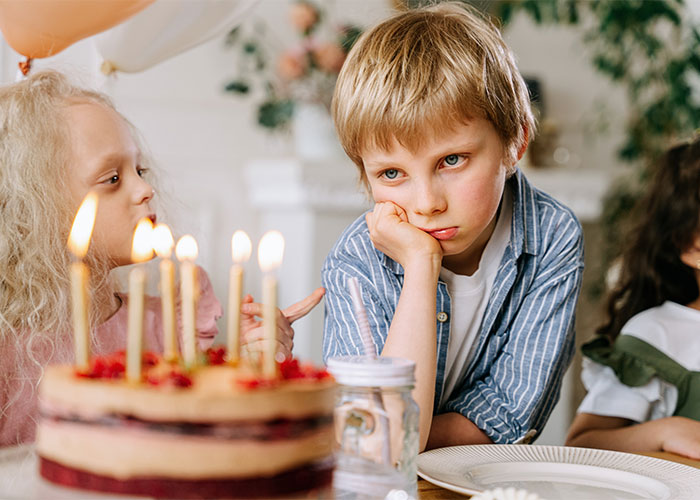 Two children at a birthday party, one boy looking bored, illustrating outdated parenting myths about children’s behavior.