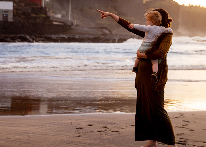 Mother holding child and pointing toward ocean waves on beach at sunset illustrating outdated parenting myths.