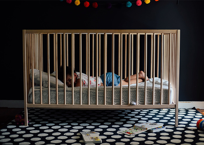 Child lying in wooden crib in dark room with toys on polka dot rug, illustrating outdated parenting myths concept.