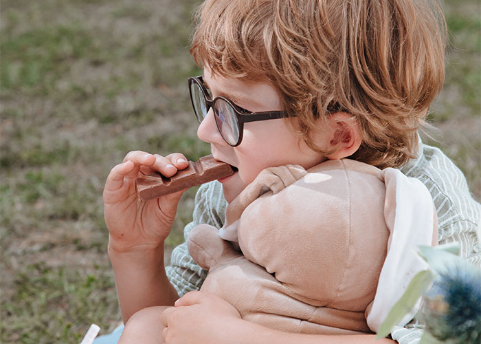 Child with glasses eating chocolate while hugging a plush toy, illustrating outdated parenting myths about treats and comfort.