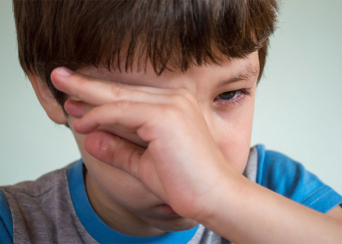 Close-up of a young boy rubbing his eyes, illustrating common issues related to outdated parenting myths.