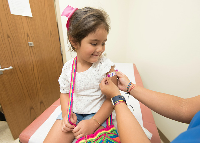 Young girl receiving a bandage on arm at doctor’s office, illustrating outdated parenting myths about childhood health and care.