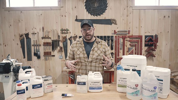 Man explaining epoxy countertop materials on a wood table in a workshop with tools on the wall behind him