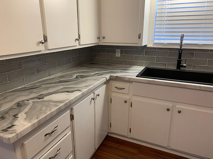 Unique epoxy countertop with marbled design in a bright white kitchen featuring subway tile backsplash and black sink.