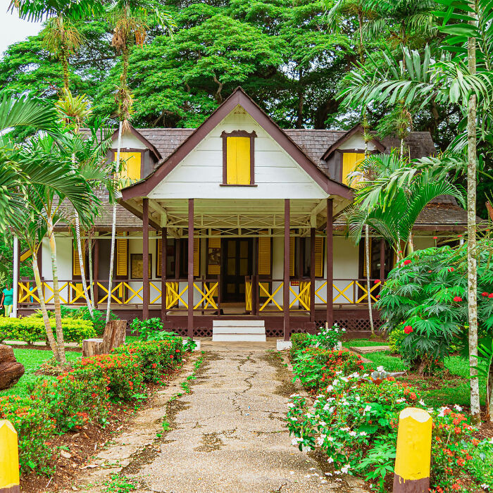 Brown wooden house surrounded by green trees and flowers