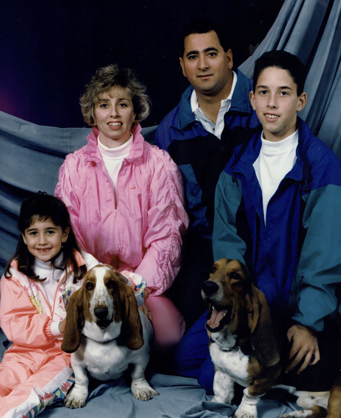 Family posing awkwardly with two dogs in colorful 90s tracksuits, capturing a humorous family photo moment.