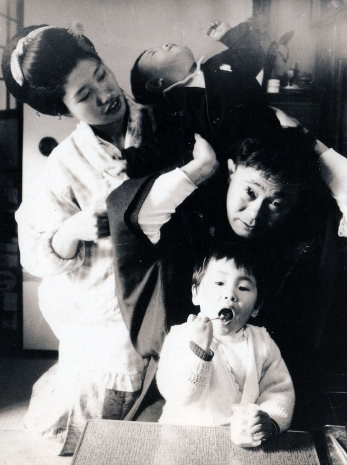Family photo with a child on dad's shoulders, mom smiling, and another child enjoying dessert.