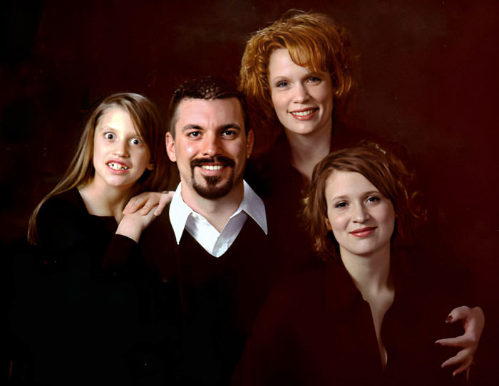 A funny family photo with four people posing awkwardly, featuring big smiles and quirky expressions.