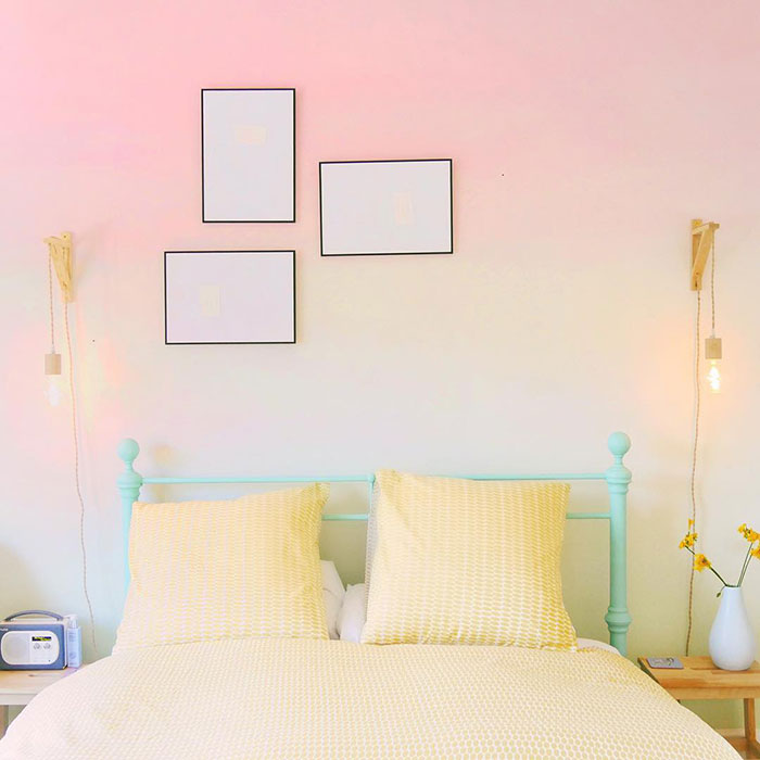 Ombre wall painting design in a bedroom with soft pink and cream gradient above a yellow bed.