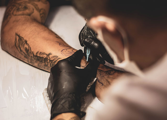 Tattoo artist in black gloves working on a floral design on a client's arm. Tattoo artist in black gloves working on a floral design on a client's arm.