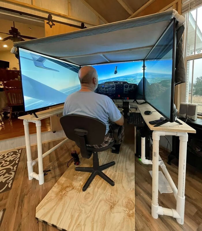 Man sitting at a cozy home office setup with three large monitors displaying a flight simulator in a wooden room.