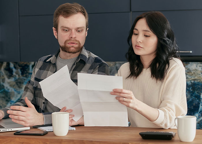 Man looks shocked reading paternity test results while wife calmly reviews papers, relating to baby's <a href=