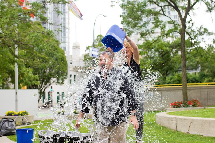 Person pouring a bucket of water on another outdoors, showing uplifting moments that prove our world isn't a total nightmare.