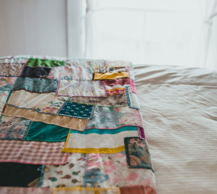 Colorful patchwork quilt neatly spread on a bed, symbolizing comfort and warmth in our world proof.