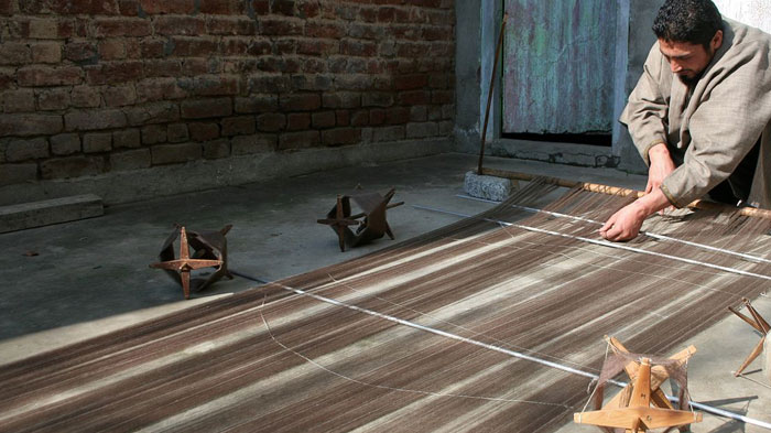 Man weaving on a loom in a rustic setting, showcasing a traditional skill rarely covered in school lessons.