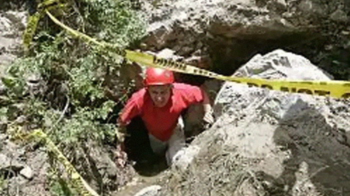 A person in a red helmet and shirt emerges from a cave, surrounded by caution tape, illustrating intriguing facts.