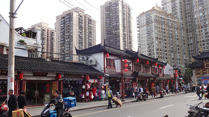 Traditional market street with bustling activity, set against modern skyscrapers in the background.
