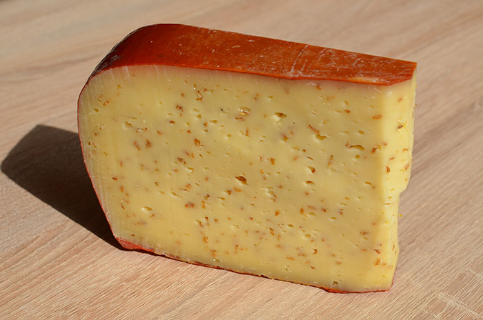 A wedge of cheese with a reddish rind on a wooden surface.