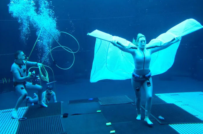 Person underwater in a swimming pool, wearing a suit with wing-like fabric, demonstrating intriguing buoyancy skills.