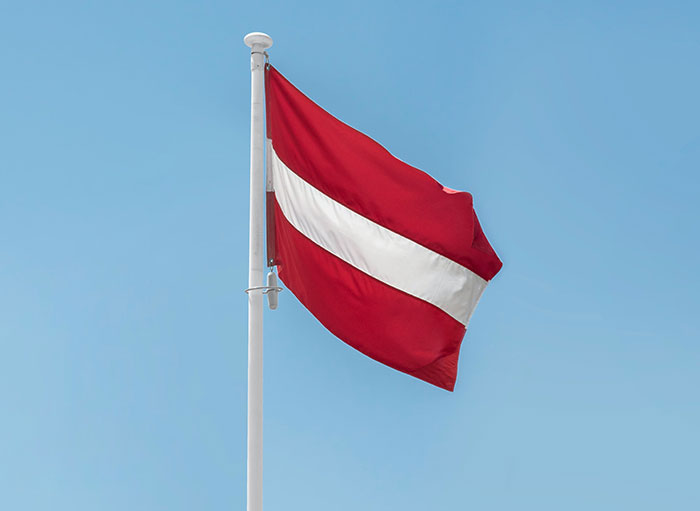 Flag of Latvia waving against a clear sky, related to intriguing facts not learned in school.