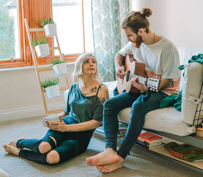 Couple enjoying a cozy moment with guitar and coffee at home, showing positive moments in our world online.