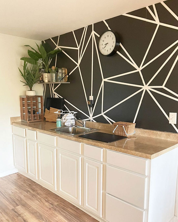 Kitchen wall painting design with black background and white geometric lines above beige countertop and cabinets.