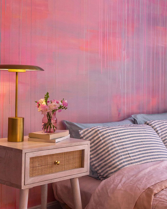 Pink wall painting design with vertical paint drips above a bedside table, striped pillows, and soft bedding in a cozy bedroom.