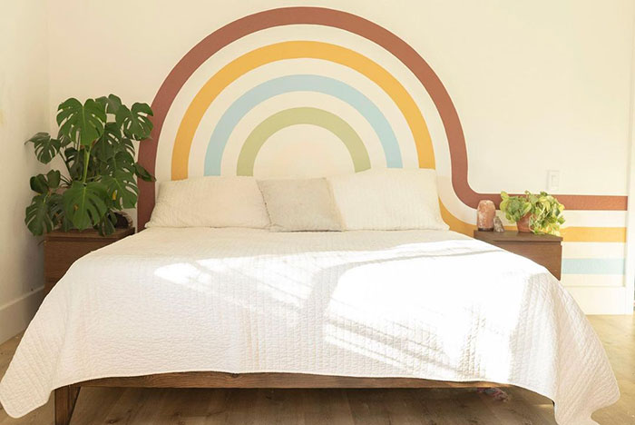 Arches wall painting design in soft earthy colors behind a bed in a bright, minimalistic bedroom setting.