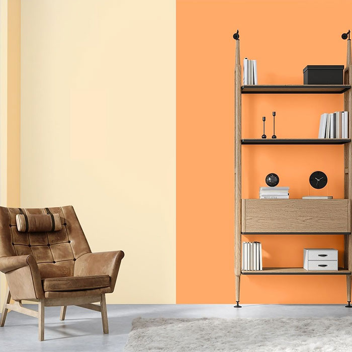 Wall painting design with beige and orange color blocks in a modern living room featuring a brown armchair and wooden shelving unit.