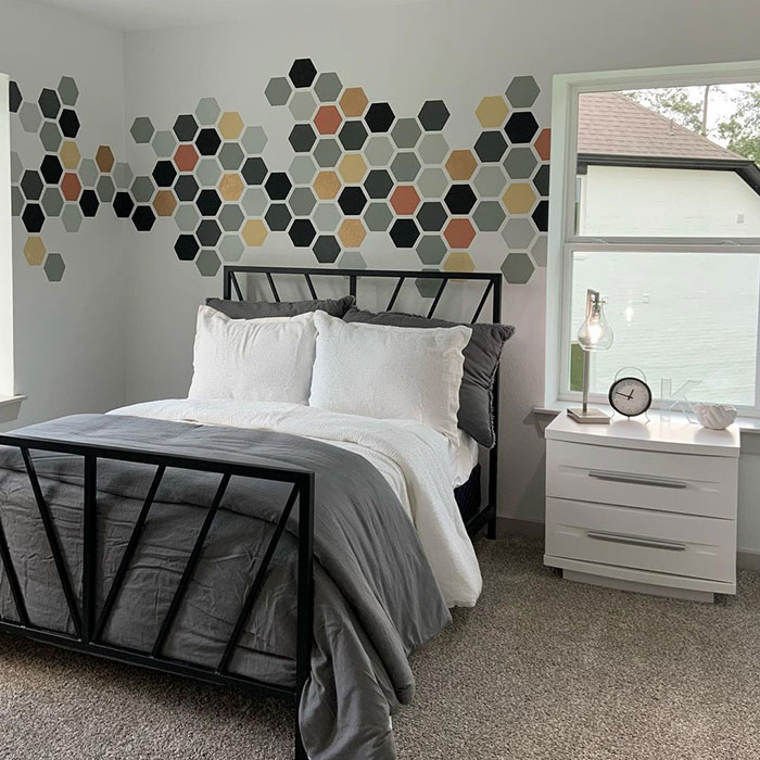 Honeycomb style bedroom wall painting design with neutral tones and modern geometric patterns above black metal bed frame.