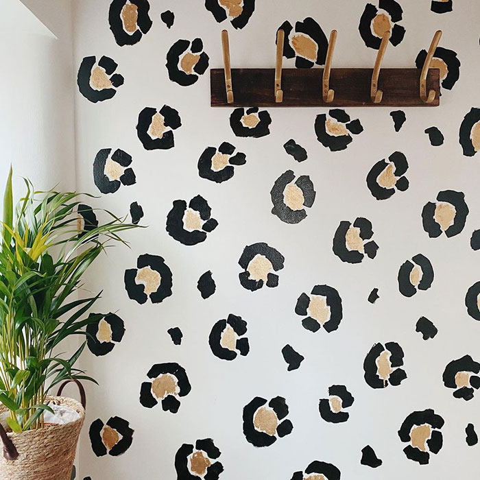 Tiger prints wall painting design on white wall with a wooden coat rack and a potted green plant nearby.