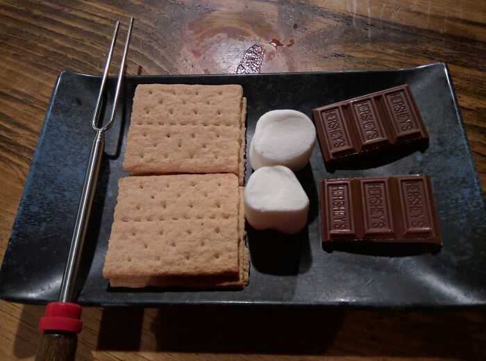 S'mores ingredients on a plate: graham crackers, marshmallows, and chocolate with a roasting fork.
