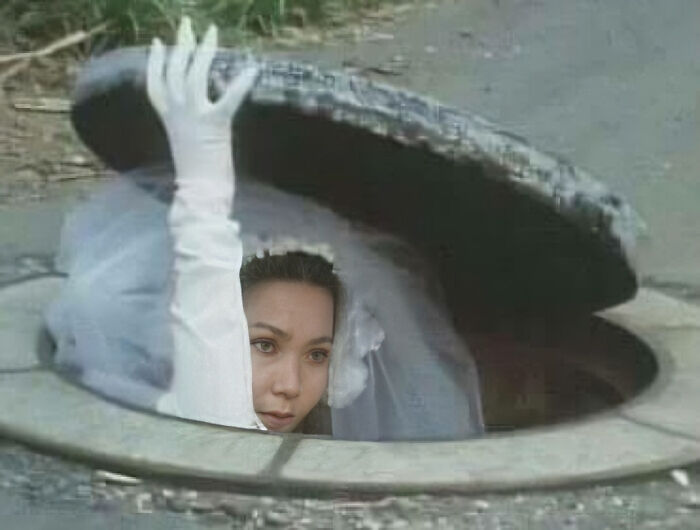 Bride humorously emerging from a manhole, wearing a white veil and glove, showcasing a funny image with no context.