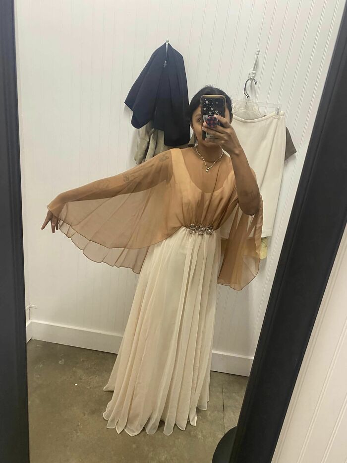 Person trying on a flowing dress in front of a mirror, showcasing a lucky thrift store fashion find.
