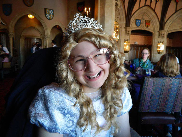 Person in costume with curly wig and tiara sitting in a themed restaurant.